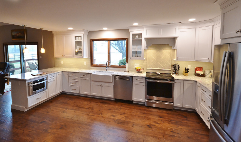Inredning av ett klassiskt stort flerfärgad flerfärgat kök, med en rustik diskho, luckor med upphöjd panel, vita skåp, granitbänkskiva, vitt stänkskydd, stänkskydd i tunnelbanekakel, rostfria vitvaror, mellanmörkt trägolv, en halv köksö och brunt golv