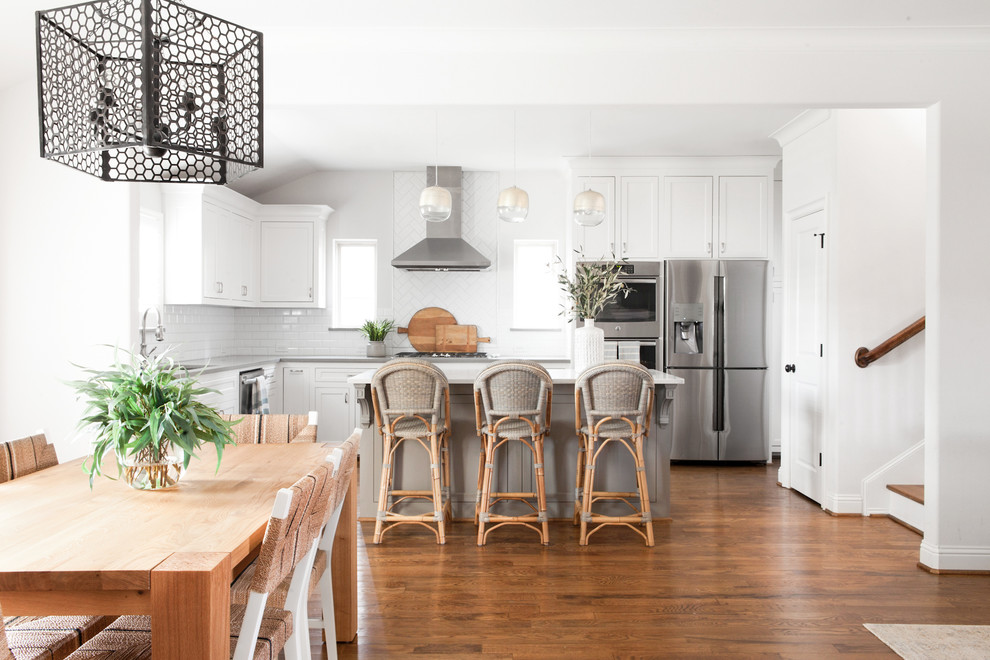 Eat-in kitchen - mid-sized transitional medium tone wood floor and brown floor eat-in kitchen idea in Dallas with a single-bowl sink, shaker cabinets, white cabinets, quartz countertops, white backsplash, ceramic backsplash, stainless steel appliances, an island and white countertops