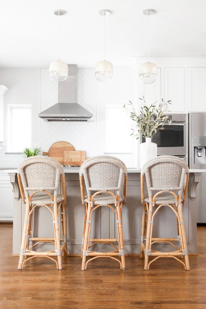 Cette image montre une cuisine ouverte traditionnelle en U de taille moyenne avec un évier 1 bac, un placard à porte shaker, des portes de placard blanches, un plan de travail en quartz modifié, une crédence blanche, une crédence en céramique, un électroménager en acier inoxydable, un sol en bois brun, îlot, un sol marron et un plan de travail blanc.