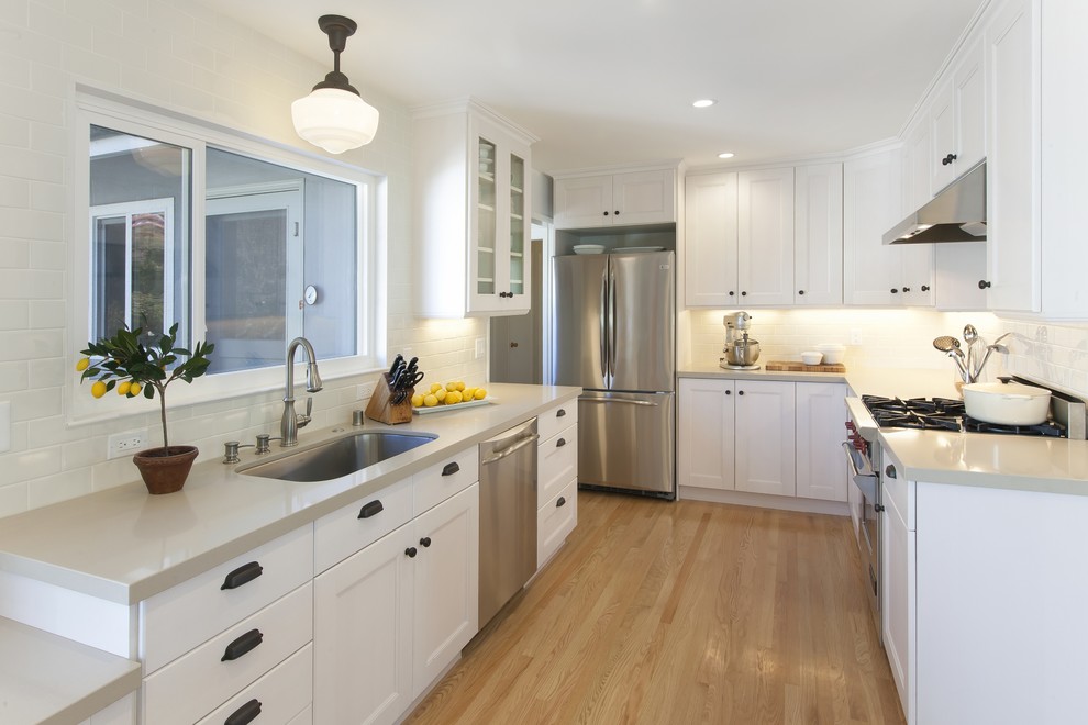 Inspiration for a mid-sized timeless l-shaped light wood floor enclosed kitchen remodel in San Francisco with an undermount sink, shaker cabinets, white cabinets, white backsplash, subway tile backsplash, stainless steel appliances and an island
