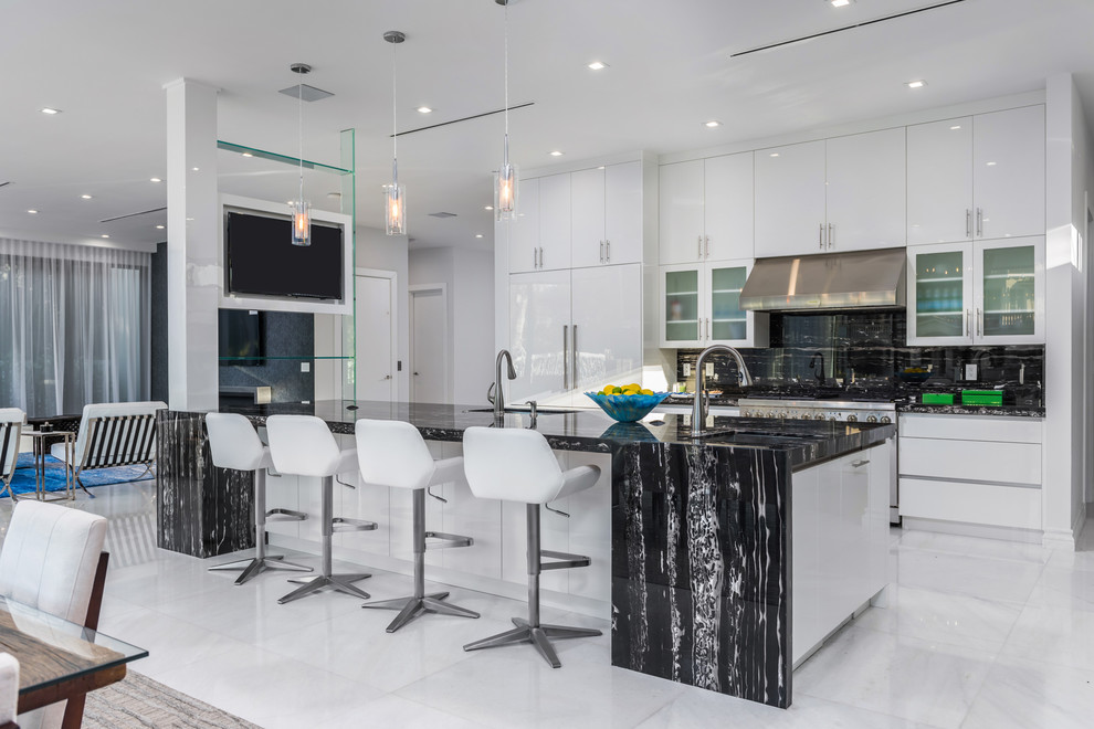 Contemporary kitchen in Miami with flat-panel cabinets, black splashback, stone slab splashback, an island, white floors, black worktops and integrated appliances.