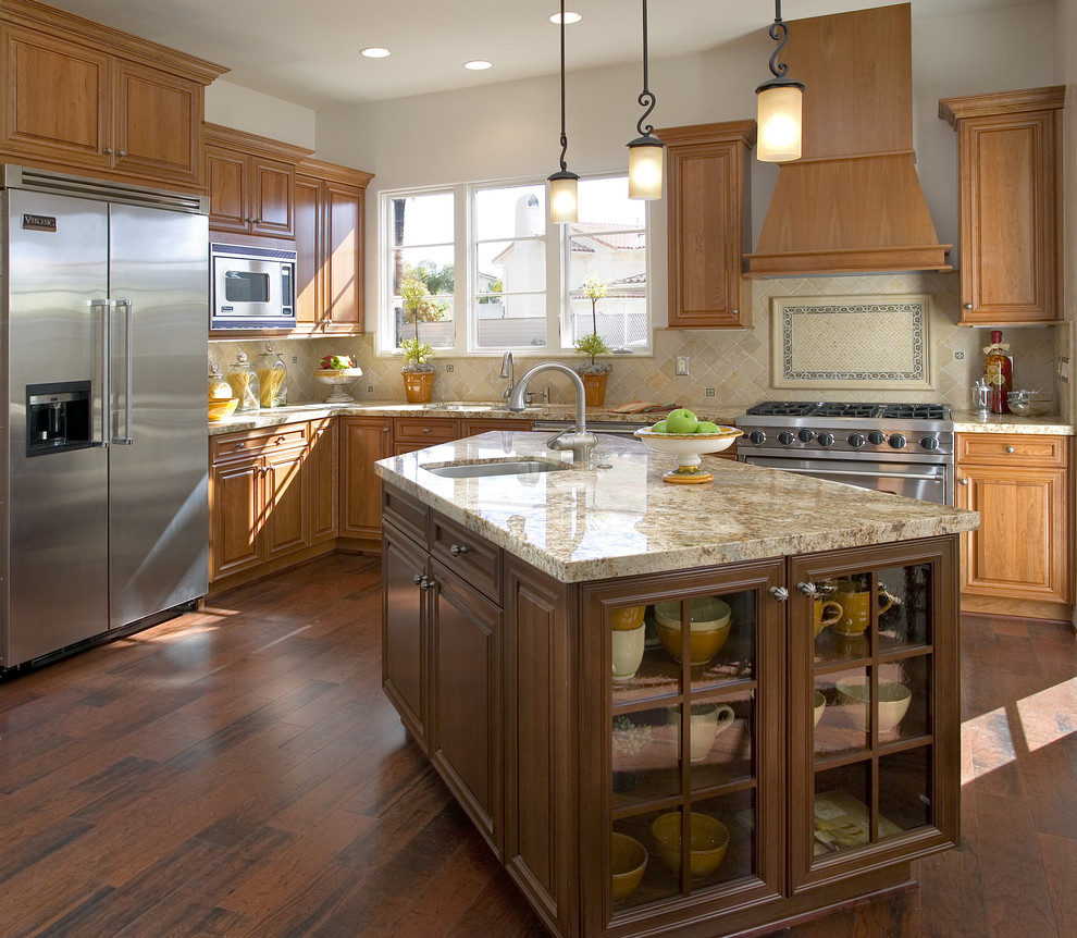 Cette photo montre une cuisine chic en L et bois brun avec un placard avec porte à panneau surélevé, un électroménager en acier inoxydable, un évier encastré et une crédence beige.