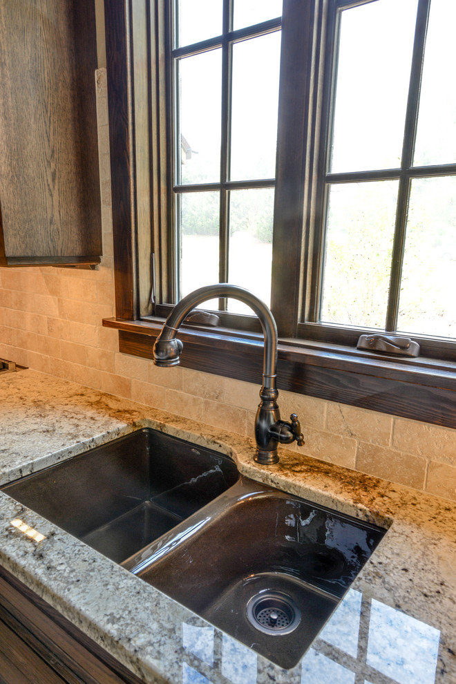 Bild på ett avskilt, stort rustikt brun brunt l-kök, med en undermonterad diskho, luckor med infälld panel, skåp i mörkt trä, granitbänkskiva, beige stänkskydd, stänkskydd i stenkakel, integrerade vitvaror, skiffergolv, en halv köksö och grått golv