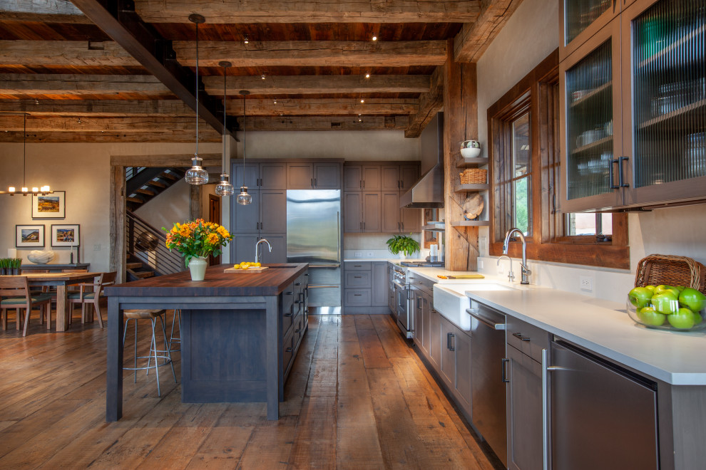 Example of a mountain style l-shaped dark wood floor, brown floor and exposed beam kitchen design in Denver with a farmhouse sink, shaker cabinets, dark wood cabinets, stainless steel appliances, an island and gray countertops
