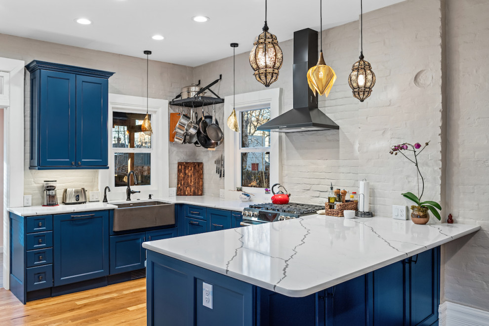 Eat-in kitchen - mid-sized eclectic u-shaped medium tone wood floor and brown floor eat-in kitchen idea in Other with a farmhouse sink, recessed-panel cabinets, blue cabinets, quartz countertops, gray backsplash, brick backsplash, colored appliances, a peninsula and white countertops