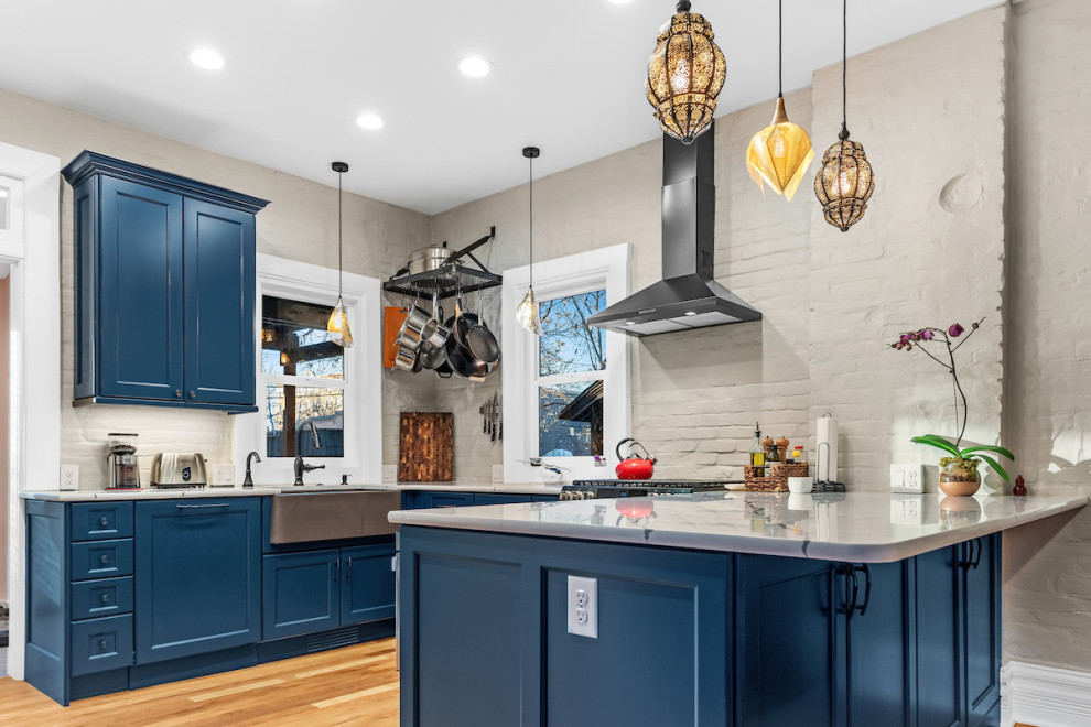 Example of a mid-sized eclectic u-shaped medium tone wood floor and brown floor eat-in kitchen design in Other with a farmhouse sink, recessed-panel cabinets, blue cabinets, quartz countertops, gray backsplash, brick backsplash, colored appliances, a peninsula and white countertops
