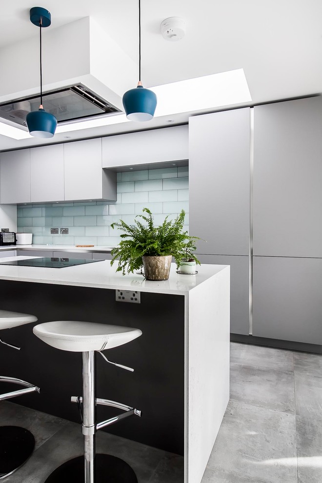 Design ideas for a medium sized contemporary galley open plan kitchen in Surrey with flat-panel cabinets, grey cabinets, composite countertops, green splashback, ceramic splashback, black appliances, an island, grey floors, a single-bowl sink and concrete flooring.