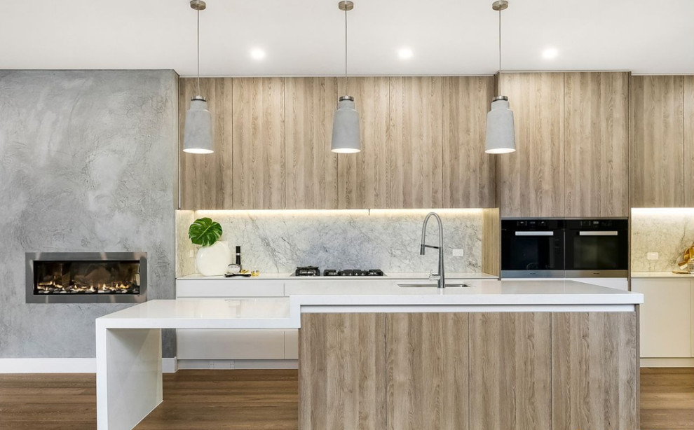 Moderne Küche mit Unterbauwaschbecken, flächenbündigen Schrankfronten, hellen Holzschränken, Küchenrückwand in Grau, Rückwand aus Marmor, schwarzen Elektrogeräten, hellem Holzboden, Kücheninsel, beigem Boden und weißer Arbeitsplatte in Melbourne