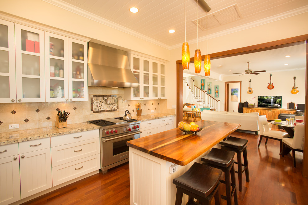 Inspiration for a mid-sized tropical galley medium tone wood floor kitchen pantry remodel in Hawaii with an undermount sink, shaker cabinets, white cabinets, granite countertops, beige backsplash, stone tile backsplash, stainless steel appliances and an island