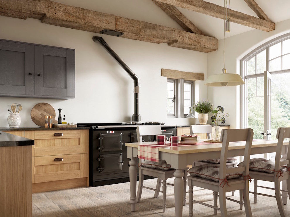 Photo of a farmhouse l-shaped kitchen/diner in Sussex with shaker cabinets, medium wood cabinets, white splashback, black appliances and light hardwood flooring.