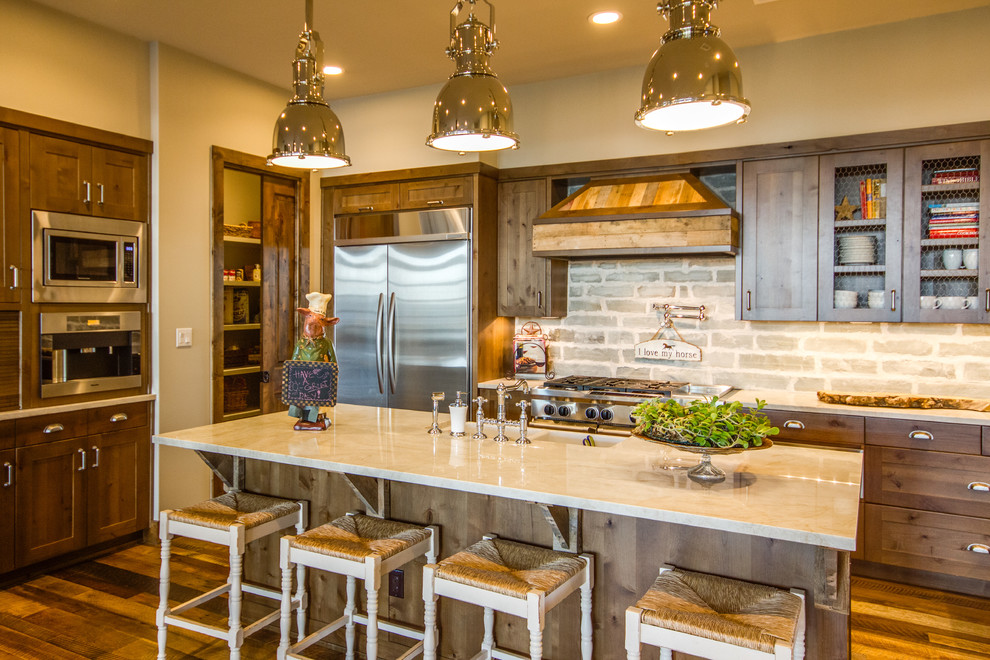 Mid-sized eclectic single-wall medium tone wood floor and brown floor eat-in kitchen photo in Austin with an island, an undermount sink, recessed-panel cabinets, medium tone wood cabinets, marble countertops, beige backsplash, stone slab backsplash, stainless steel appliances and gray countertops