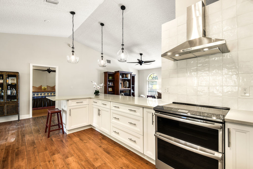 Exempel på ett mellanstort modernt vit vitt kök, med en trippel diskho, luckor med infälld panel, vita skåp, bänkskiva i kvarts, vitt stänkskydd, stänkskydd i porslinskakel, rostfria vitvaror, laminatgolv, en halv köksö och brunt golv