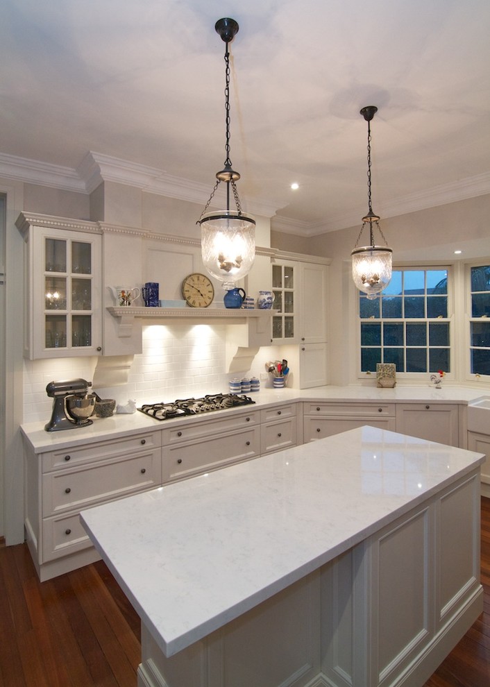 Foto på ett stort lantligt kök, med en rustik diskho, luckor med infälld panel, vita skåp, bänkskiva i kvarts, vitt stänkskydd, stänkskydd i porslinskakel, rostfria vitvaror, mörkt trägolv och en köksö