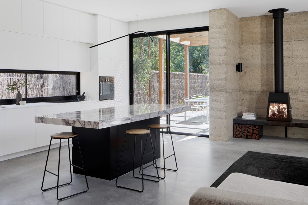 This is an example of a medium sized contemporary galley open plan kitchen in Melbourne with a submerged sink, flat-panel cabinets, white cabinets, marble worktops, black appliances, concrete flooring, an island, grey floors and white worktops.