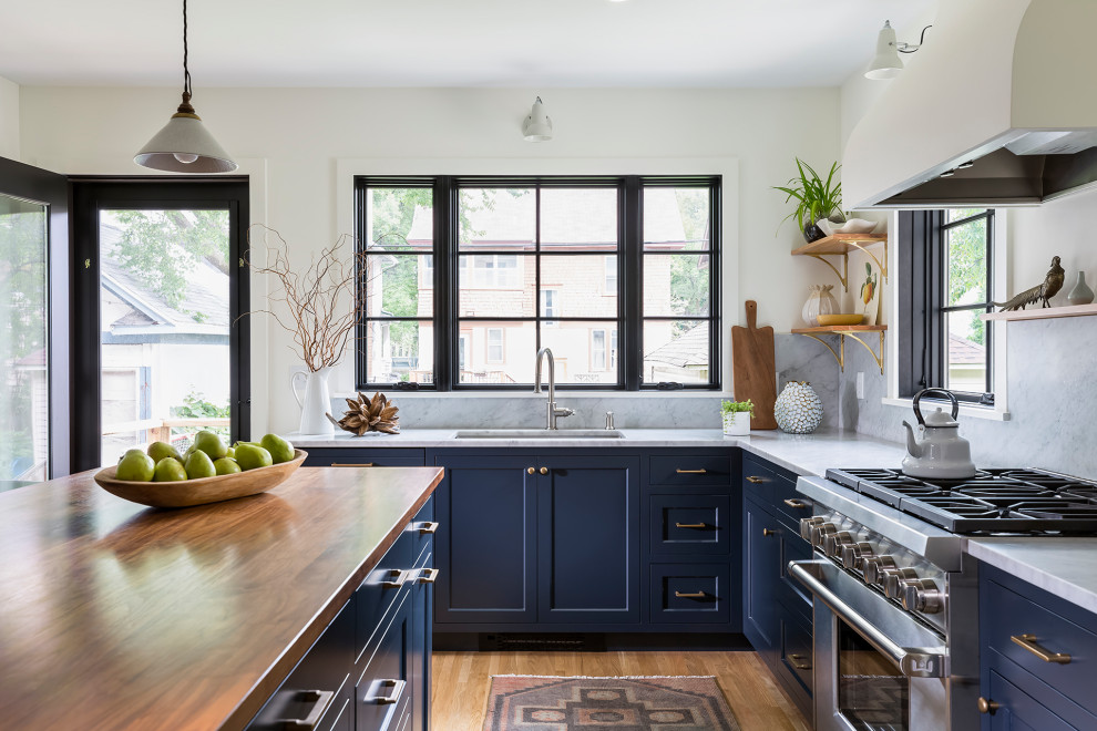 Mid-sized farmhouse l-shaped medium tone wood floor and white floor kitchen photo in Minneapolis with an undermount sink, recessed-panel cabinets, blue cabinets, wood countertops, white backsplash, marble backsplash, stainless steel appliances, an island and brown countertops