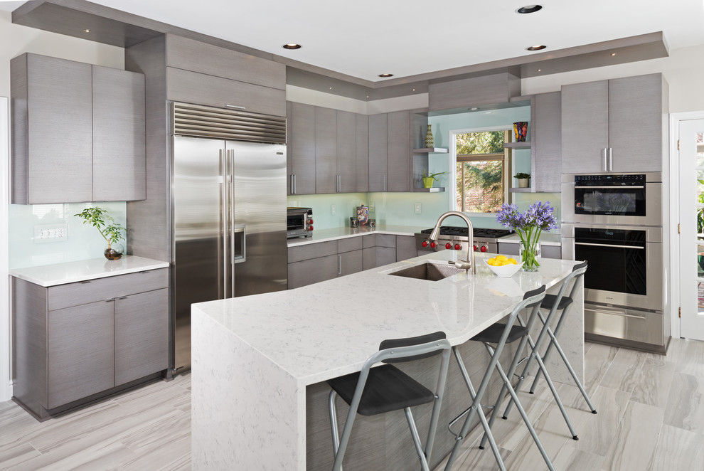 Bild på ett mellanstort funkis kök, med en undermonterad diskho, släta luckor, grå skåp, blått stänkskydd, glaspanel som stänkskydd, rostfria vitvaror, en köksö, bänkskiva i kvarts, klinkergolv i porslin och grått golv
