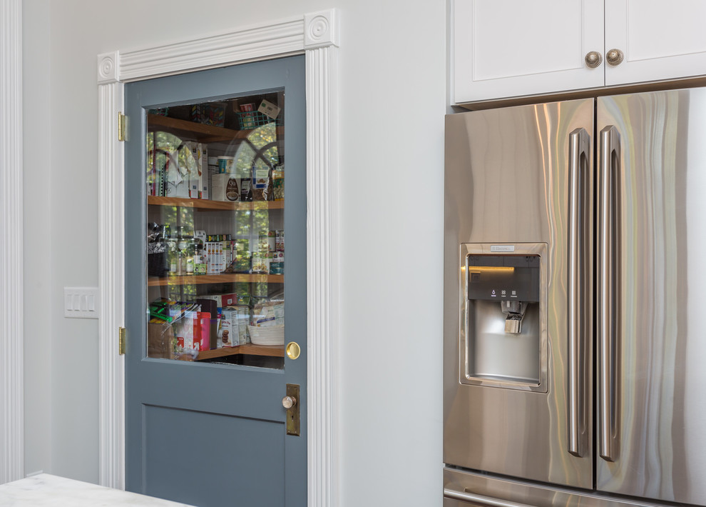 Photo of a large traditional u-shaped kitchen pantry in Raleigh with a belfast sink, shaker cabinets, white cabinets, marble worktops, white splashback, marble splashback, stainless steel appliances, dark hardwood flooring, an island, brown floors and white worktops.