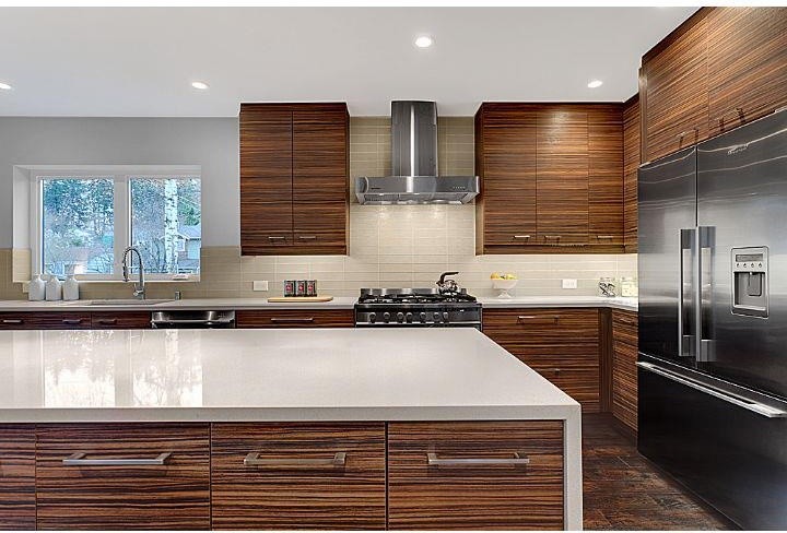 This is an example of a large contemporary l-shaped kitchen in Seattle with a submerged sink, flat-panel cabinets, dark wood cabinets, composite countertops, beige splashback, glass tiled splashback, stainless steel appliances, dark hardwood flooring, an island, brown floors and white worktops.