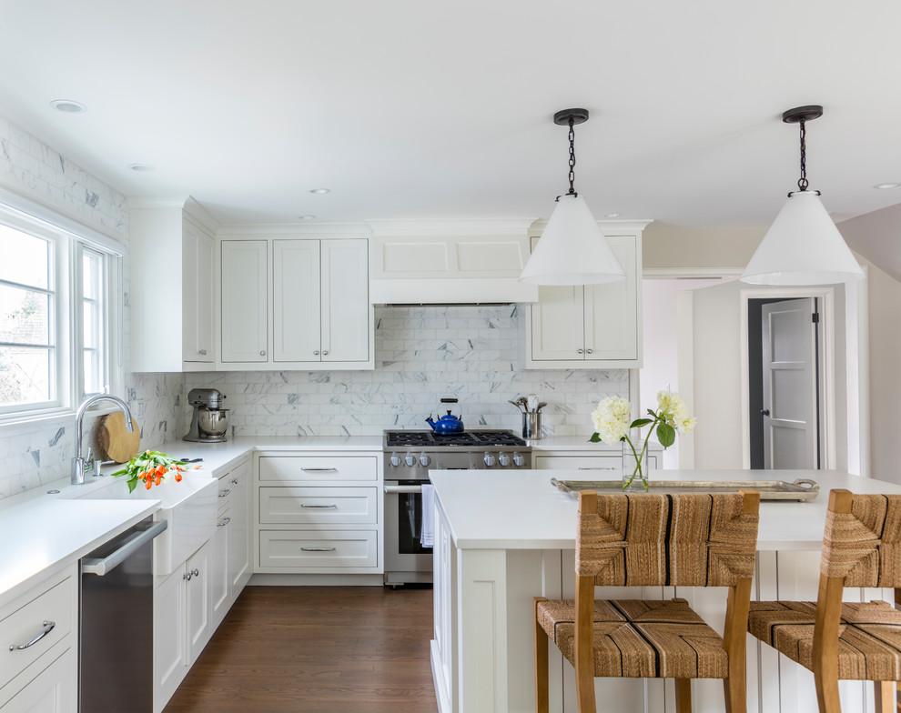 Mid-sized transitional l-shaped medium tone wood floor and brown floor open concept kitchen photo in Seattle with a farmhouse sink, shaker cabinets, white cabinets, quartz countertops, white backsplash, marble backsplash, stainless steel appliances and an island
