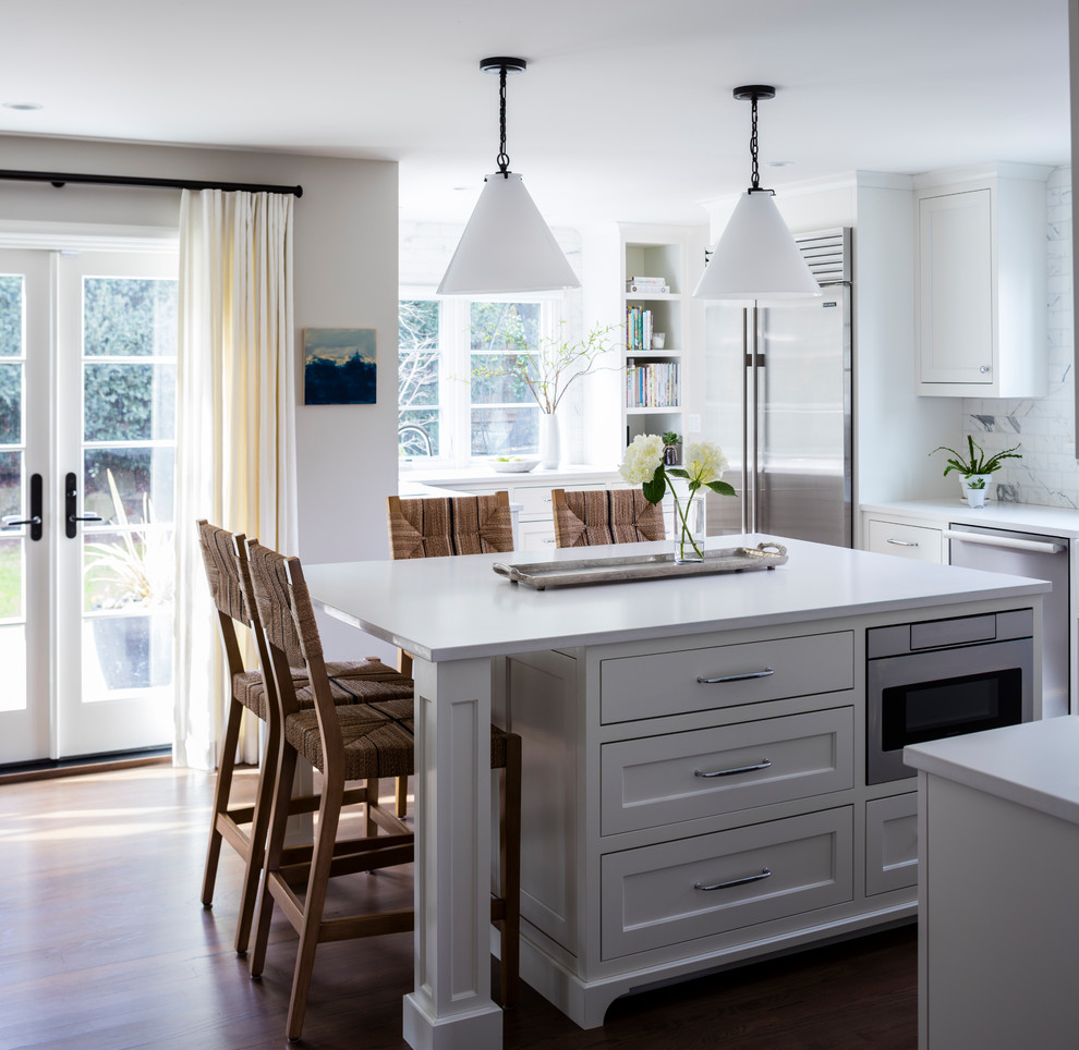 Inredning av ett klassiskt mellanstort kök, med en rustik diskho, skåp i shakerstil, vita skåp, bänkskiva i kvarts, vitt stänkskydd, stänkskydd i marmor, rostfria vitvaror, mellanmörkt trägolv, en köksö och brunt golv