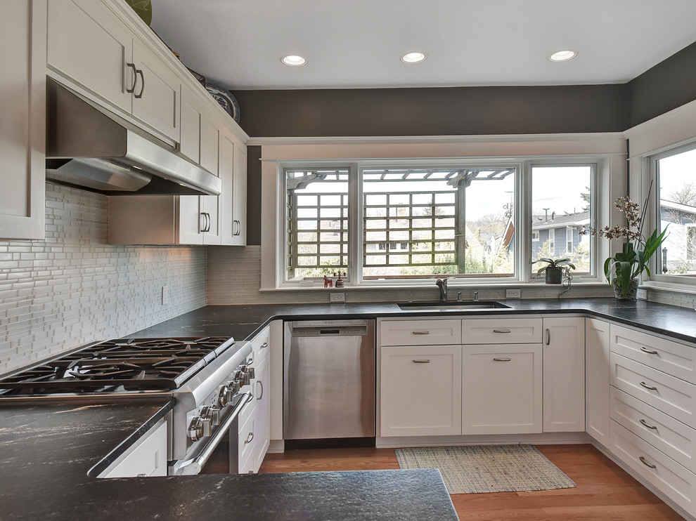 Eat-in kitchen - mid-sized transitional u-shaped medium tone wood floor and brown floor eat-in kitchen idea in Portland with an undermount sink, shaker cabinets, white cabinets, soapstone countertops, white backsplash, glass tile backsplash, stainless steel appliances and a peninsula