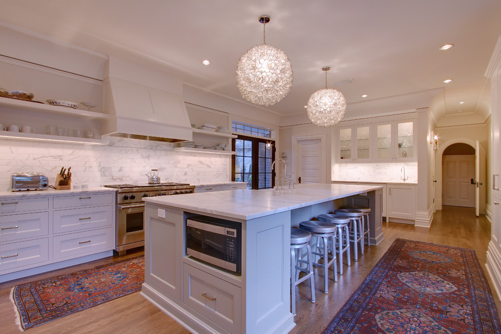 Design ideas for a large traditional enclosed kitchen in Seattle with a belfast sink, raised-panel cabinets, white cabinets, composite countertops, white splashback, metro tiled splashback, stainless steel appliances, medium hardwood flooring and an island.