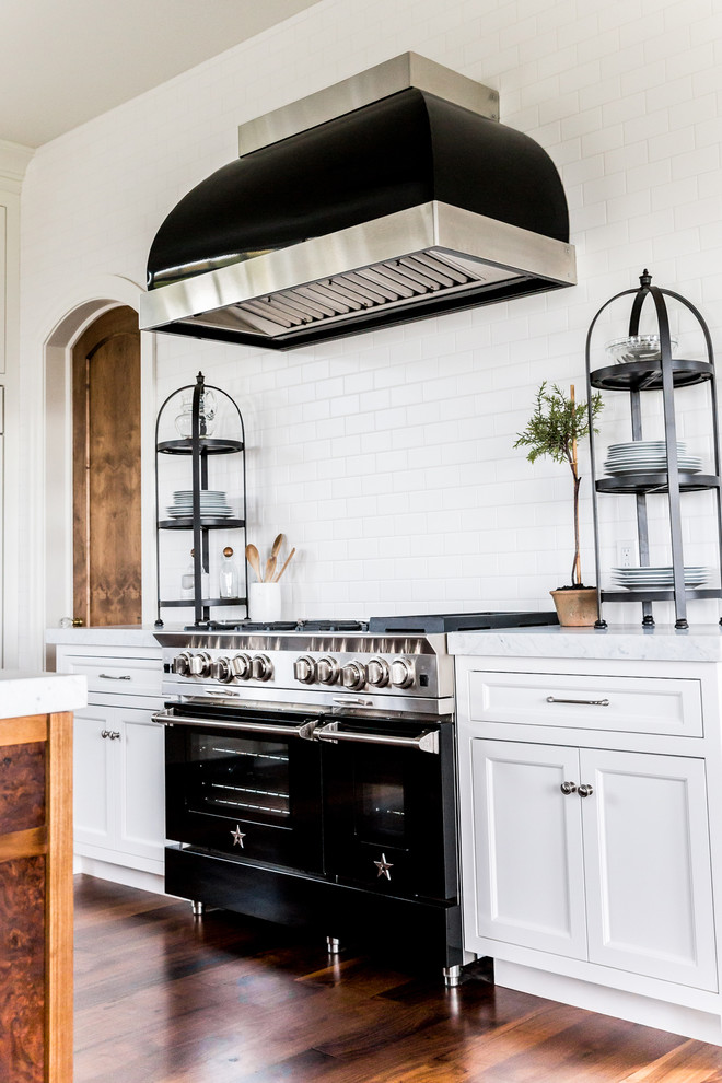Inspiration for a large transitional l-shaped medium tone wood floor eat-in kitchen remodel in Salt Lake City with a farmhouse sink, recessed-panel cabinets, white cabinets, marble countertops, white backsplash, subway tile backsplash, black appliances and an island