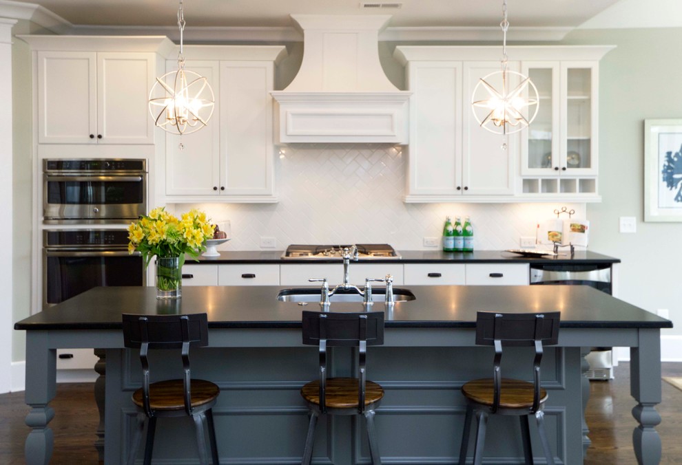 Photo of a large traditional galley open plan kitchen in Wilmington with a submerged sink, recessed-panel cabinets, white cabinets, white splashback, stainless steel appliances, dark hardwood flooring, an island, soapstone worktops, metro tiled splashback and brown floors.