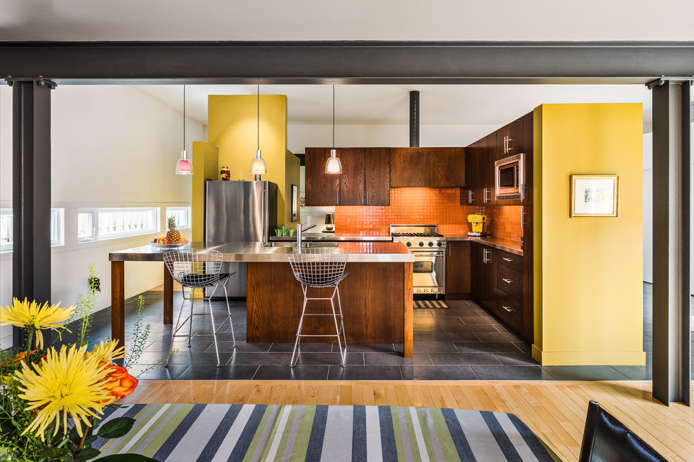 Modern inredning av ett grå grått l-kök, med en integrerad diskho, släta luckor, skåp i mörkt trä, bänkskiva i rostfritt stål, orange stänkskydd, stänkskydd i mosaik, rostfria vitvaror, en köksö och grått golv