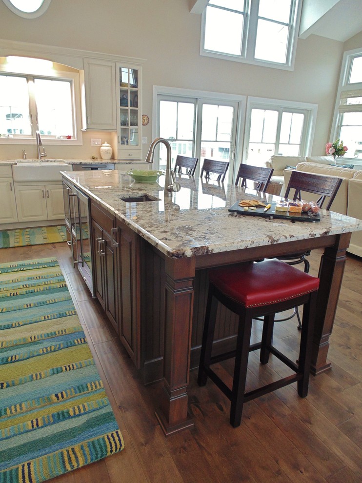 Inspiration for a mid-sized transitional l-shaped medium tone wood floor eat-in kitchen remodel in New York with a farmhouse sink, raised-panel cabinets, white cabinets, granite countertops, beige backsplash, stainless steel appliances and an island