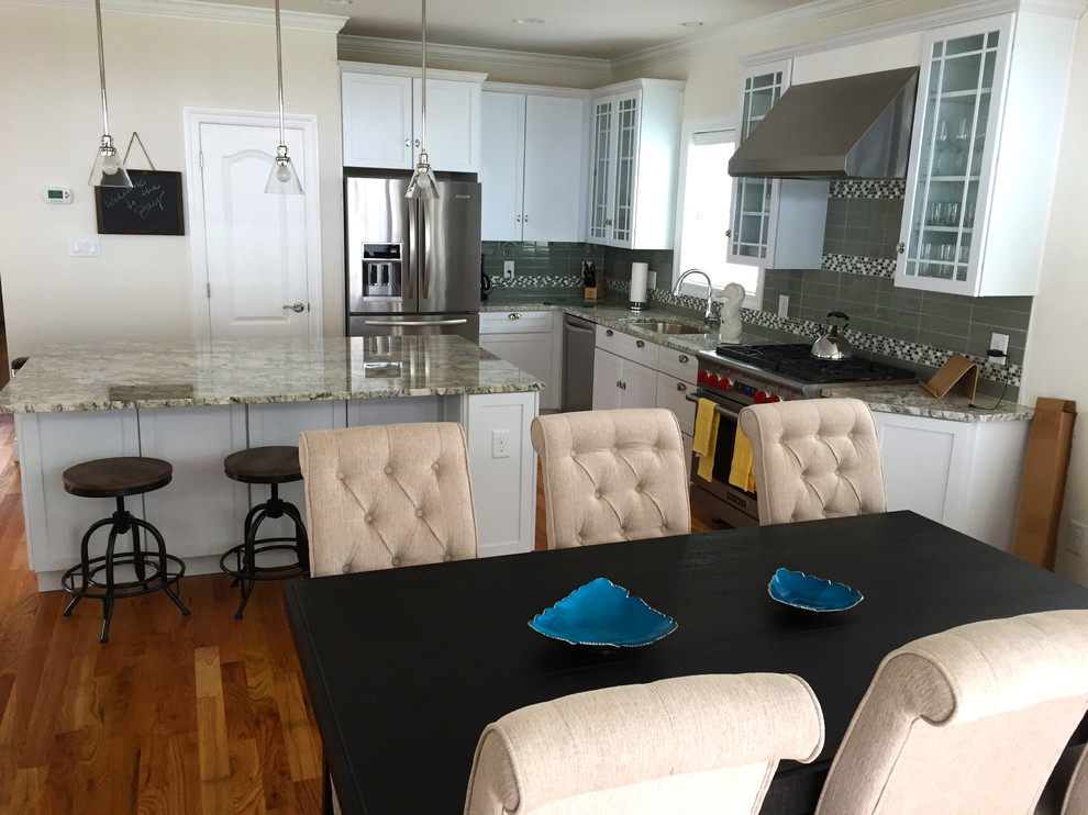 Maritime Wohnküche in L-Form mit weißen Schränken, Granit-Arbeitsplatte, Küchenrückwand in Grau, braunem Holzboden und Kücheninsel in Sonstige