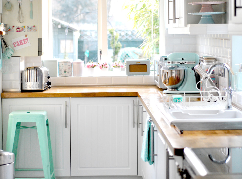 デヴォンにある中くらいなエクレクティックスタイルのおしゃれなキッチン (サブウェイタイルのキッチンパネル、木材カウンター、白いキャビネット、白いキッチンパネル、シルバーの調理設備、アイランドなし) の写真