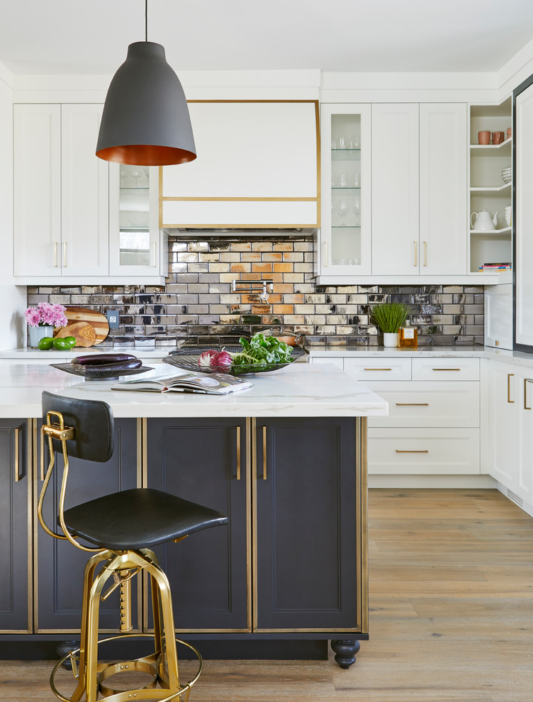 This is an example of a traditional l-shaped kitchen in Toronto with shaker cabinets, white cabinets, metallic splashback, metro tiled splashback, medium hardwood flooring, an island, brown floors and white worktops.