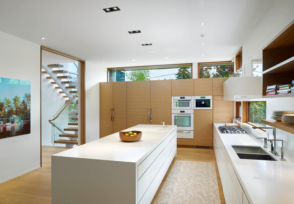 Large contemporary l-shaped open plan kitchen in Toronto with a submerged sink, flat-panel cabinets, white cabinets, composite countertops, white splashback, white appliances, light hardwood flooring and an island.