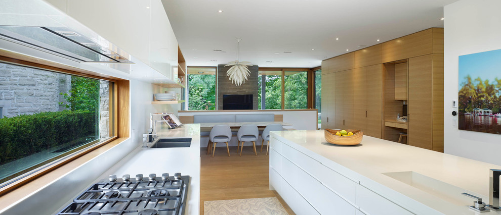 Foto di una grande cucina moderna con lavello sottopiano, ante lisce, ante bianche, top in superficie solida, paraspruzzi bianco, elettrodomestici bianchi e parquet chiaro