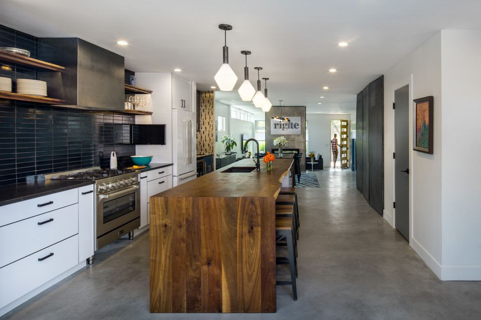 Inspiration for a mid-sized modern galley concrete floor and gray floor eat-in kitchen remodel in Denver with an undermount sink, flat-panel cabinets, white cabinets, wood countertops, black backsplash, ceramic backsplash, stainless steel appliances and an island