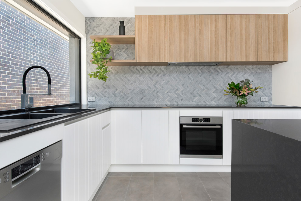 Foto på ett funkis grå l-kök, med en nedsänkt diskho, släta luckor, vita skåp, grått stänkskydd, rostfria vitvaror, en köksö och grått golv