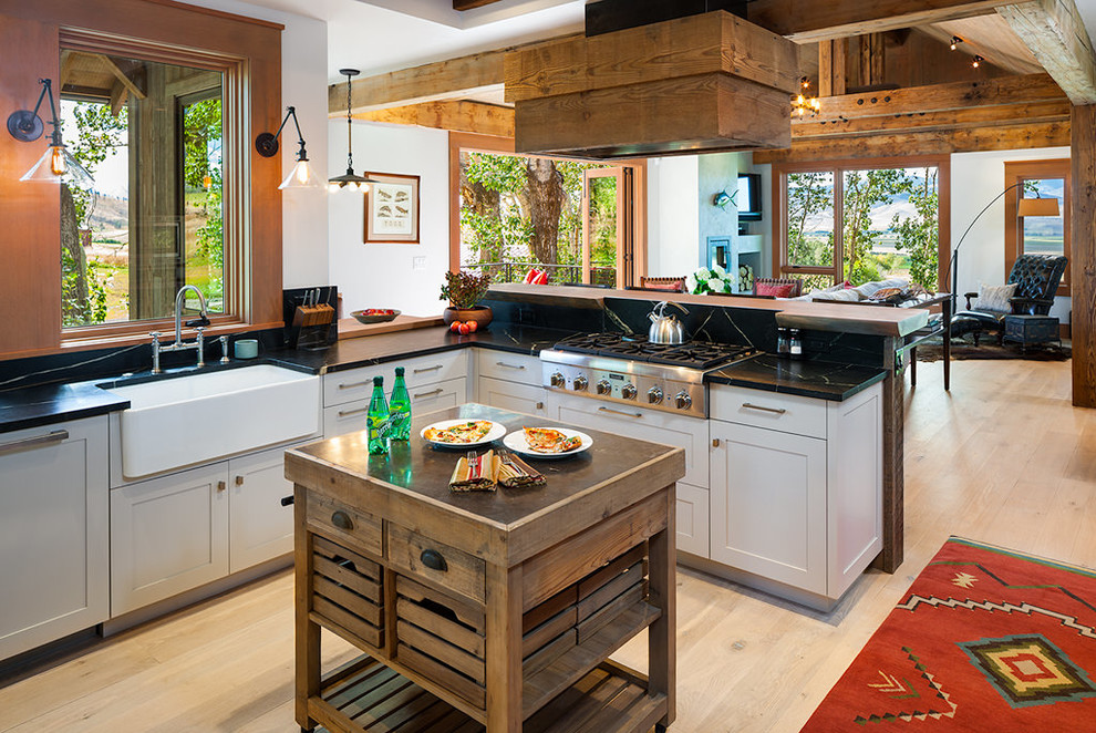 Design ideas for a rustic open plan kitchen in Other with a belfast sink, shaker cabinets, white cabinets, stainless steel appliances, light hardwood flooring and an island.