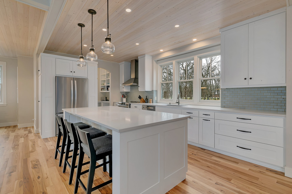 Idéer för ett mellanstort klassiskt vit kök, med en undermonterad diskho, skåp i shakerstil, vita skåp, bänkskiva i kvartsit, blått stänkskydd, stänkskydd i glaskakel, rostfria vitvaror, mellanmörkt trägolv, en köksö och brunt golv