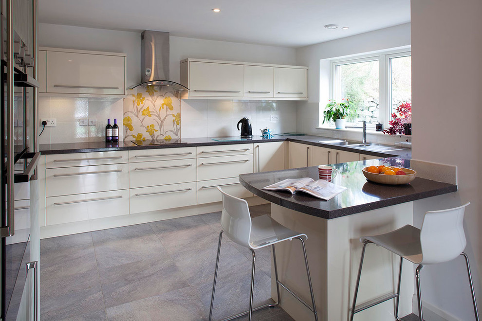 Small contemporary u-shaped kitchen in Cornwall with an integrated sink, flat-panel cabinets, white cabinets, composite countertops, white splashback, ceramic flooring and a breakfast bar.