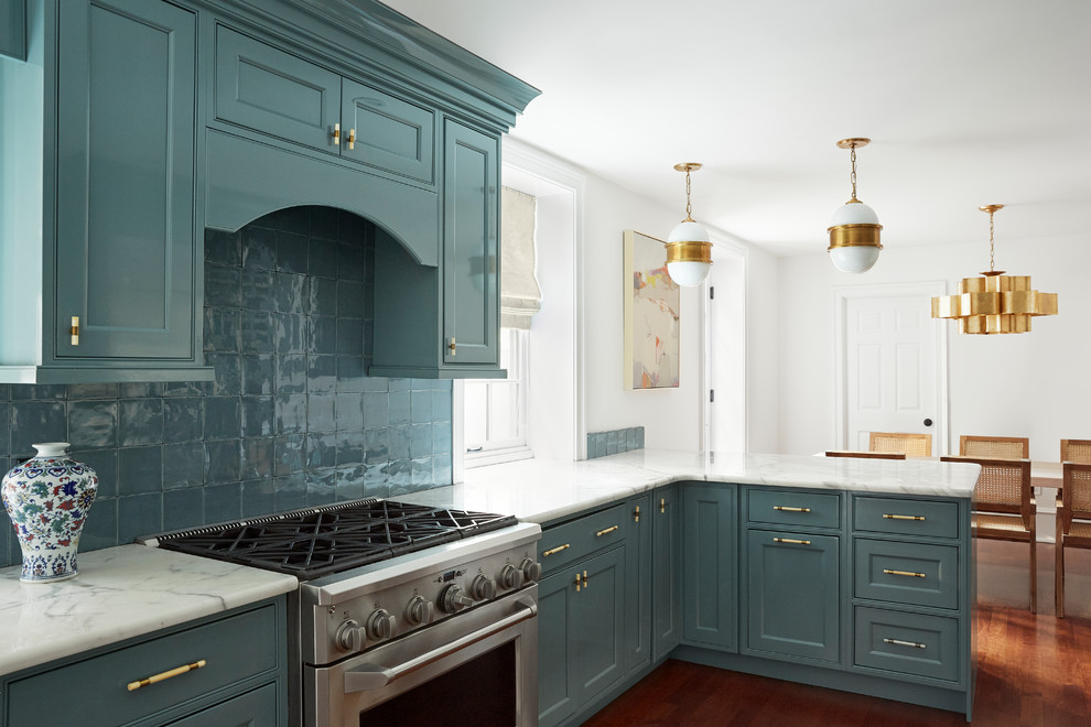 Cette photo montre une cuisine chic avec un placard à porte affleurante, des portes de placard bleues, une crédence bleue, un électroménager en acier inoxydable, un sol en bois brun, une péninsule, un sol marron et un plan de travail blanc.