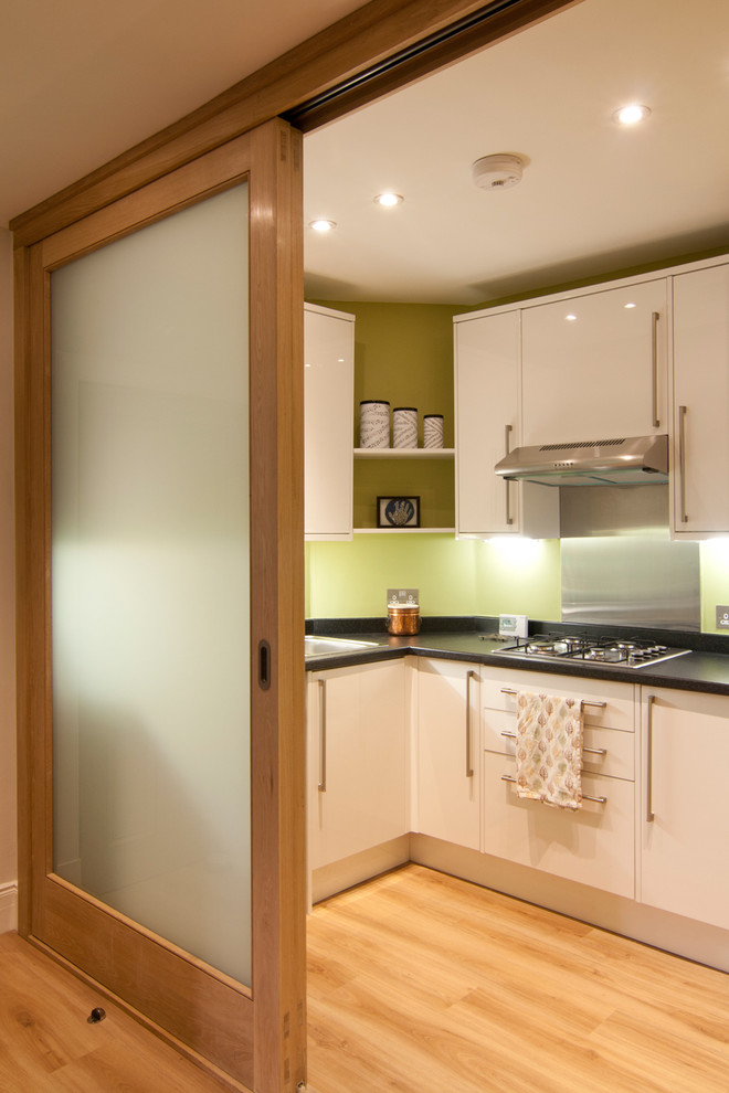 エディンバラにある小さなコンテンポラリースタイルのおしゃれなキッチン (フラットパネル扉のキャビネット、白いキャビネット、無垢フローリング、ステンレスのキッチンパネル) の写真