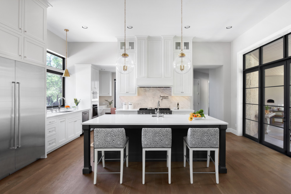 Inspiration for a traditional l-shaped kitchen in Austin with a submerged sink, shaker cabinets, white cabinets, white splashback, stone slab splashback, medium hardwood flooring, an island, brown floors and white worktops.