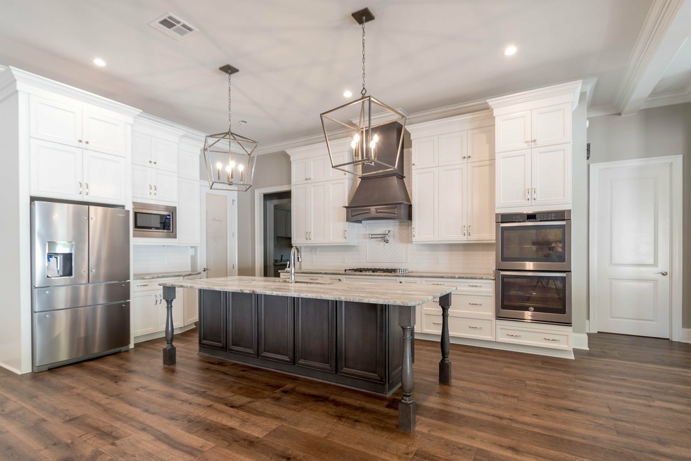 Kitchen - traditional dark wood floor and brown floor kitchen idea in New Orleans with a farmhouse sink, granite countertops, white backsplash, stainless steel appliances, an island and beige countertops