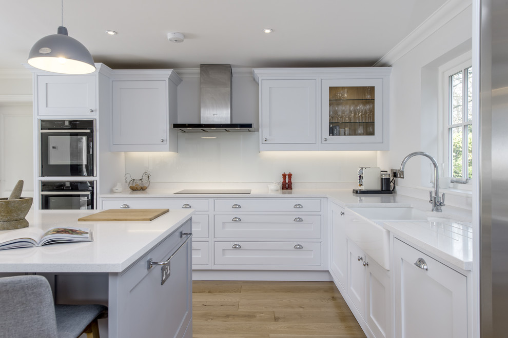 Photo of a medium sized classic l-shaped open plan kitchen in Surrey with a belfast sink, shaker cabinets, quartz worktops, glass sheet splashback and an island.