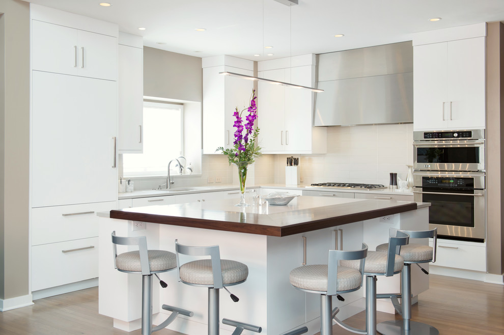 Example of a mid-sized trendy l-shaped light wood floor eat-in kitchen design in Kansas City with an undermount sink, flat-panel cabinets, white cabinets, quartz countertops, gray backsplash, ceramic backsplash, stainless steel appliances and an island