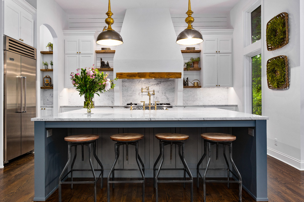 This is an example of a large classic l-shaped kitchen in Kansas City with recessed-panel cabinets, white cabinets, white splashback, marble splashback, stainless steel appliances, dark hardwood flooring, an island, white worktops and brown floors.