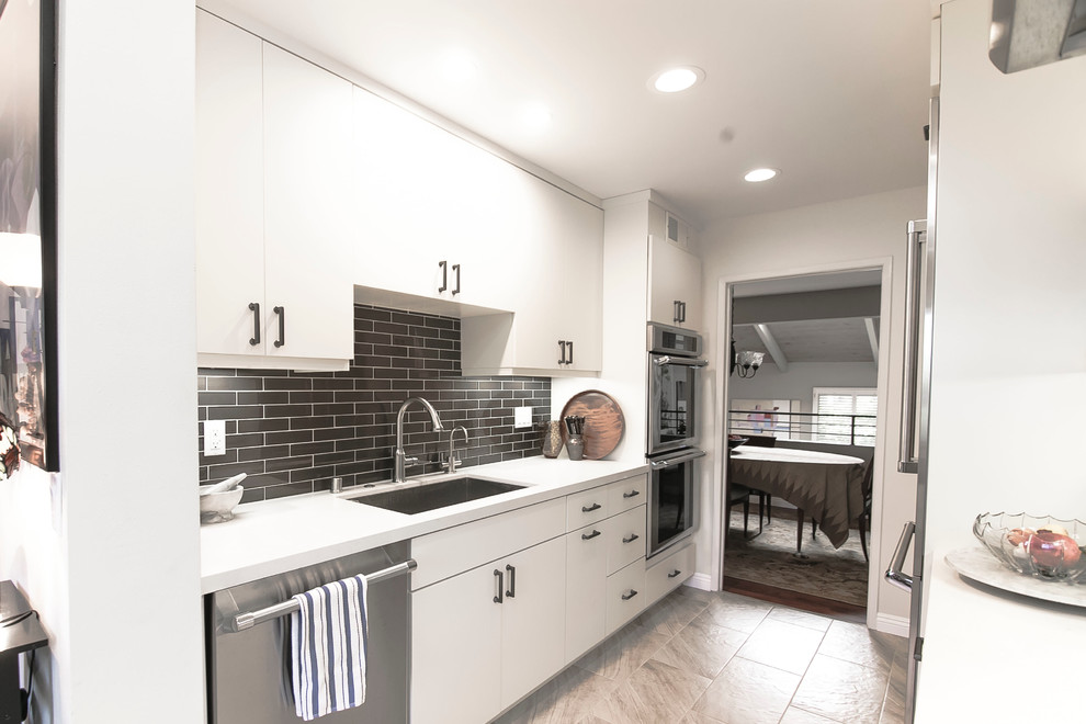 Photo of a medium sized modern galley kitchen pantry in Los Angeles with a built-in sink, flat-panel cabinets, white cabinets, engineered stone countertops, brown splashback, metro tiled splashback, stainless steel appliances, ceramic flooring and no island.