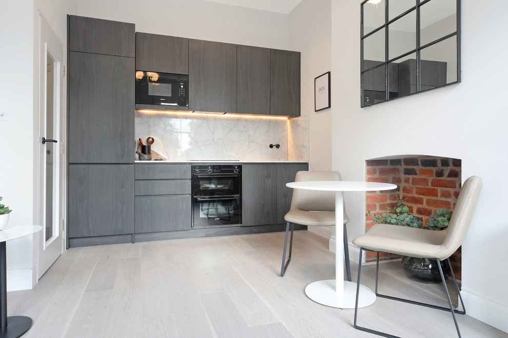 Einzeilige Moderne Wohnküche ohne Insel mit flächenbündigen Schrankfronten, grauen Schränken, Küchenrückwand in Weiß, schwarzen Elektrogeräten und grauem Boden in London