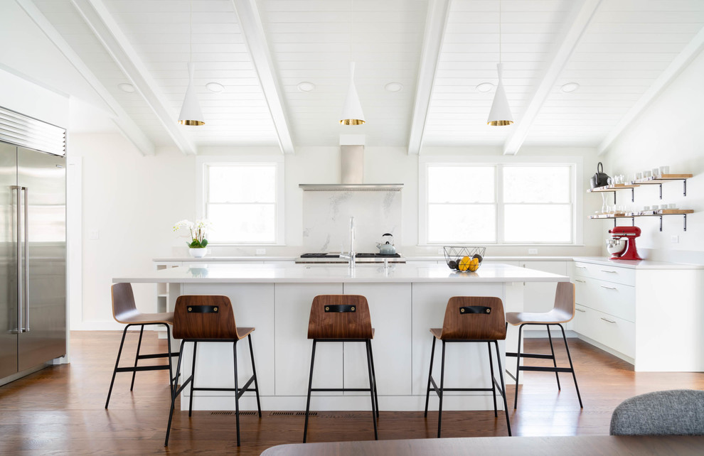 Inspiration for a medium sized country l-shaped kitchen/diner in Boston with a single-bowl sink, flat-panel cabinets, white cabinets, engineered stone countertops, white splashback, stone slab splashback, stainless steel appliances, dark hardwood flooring, an island, brown floors and white worktops.